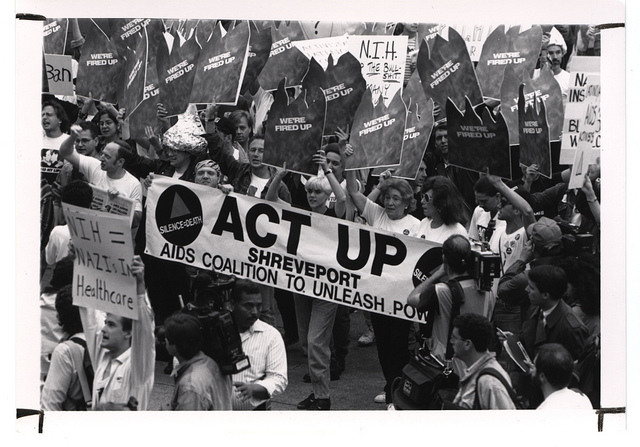 Black and white photo of activists holding signs reading "NIH=Nazis In Healthcare" and "We're fired up."