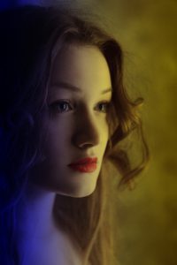 Young woman with warm yellow light on her right side of face and cold blue light on left.