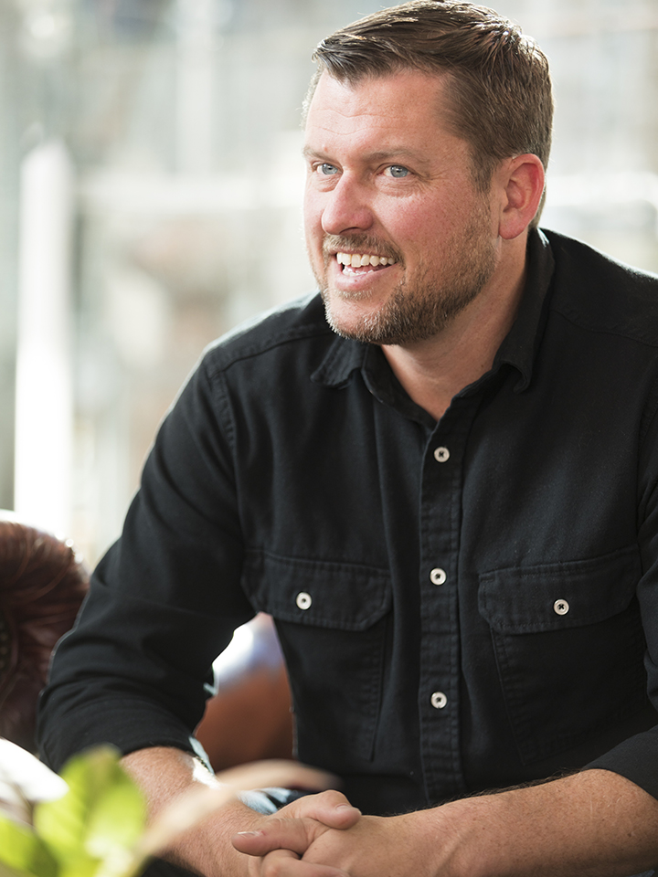 Photo of a smiling man with short light brown hair wearing a black button-down shirt.