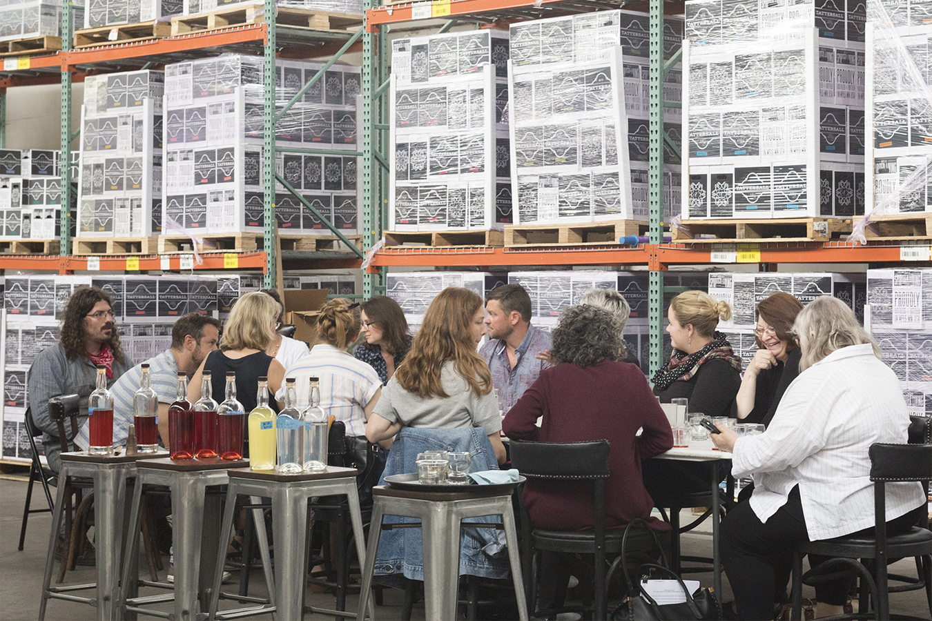 Photo of a group of people sitting at a long table with several bottles of liquor nearby.