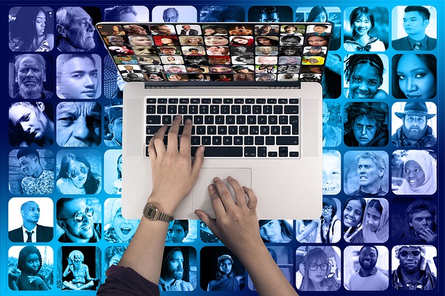 Two hands typing on a laptop seen from above. A collage of many faces fill the background.